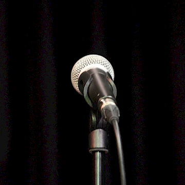 An SM58 handheld microphone on a stand against a black background.