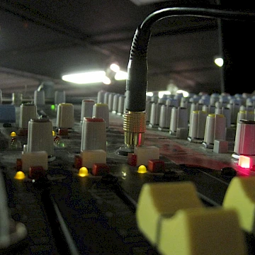 Photo of an Allen & Heath analog sound console taken from below the faders angled up towards the top of the console. There is a cable coming out of the console in the center of the image.